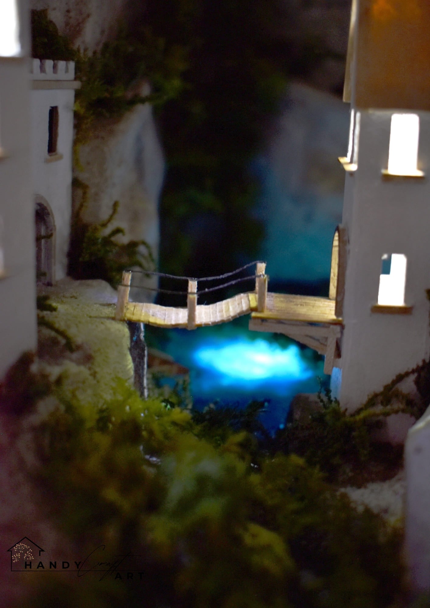 Booknook with a coastal scene with buildings and a glowing blue pool at night.