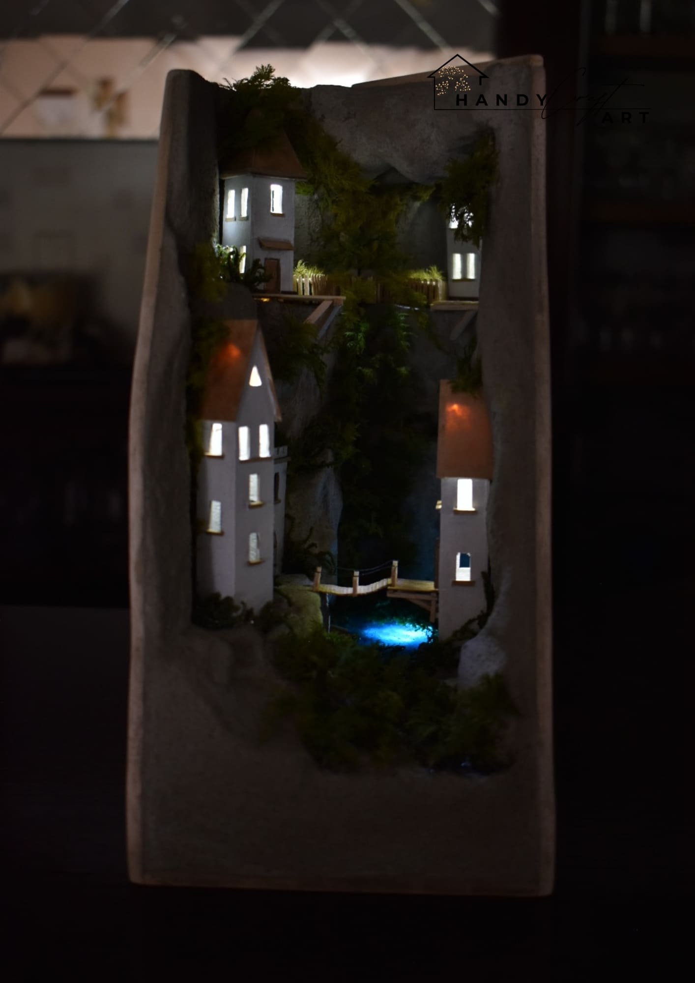 Decorative diorama with houses and lights inside a stone frame. Handmade Booknook White City on The Cliffs with lightening.
