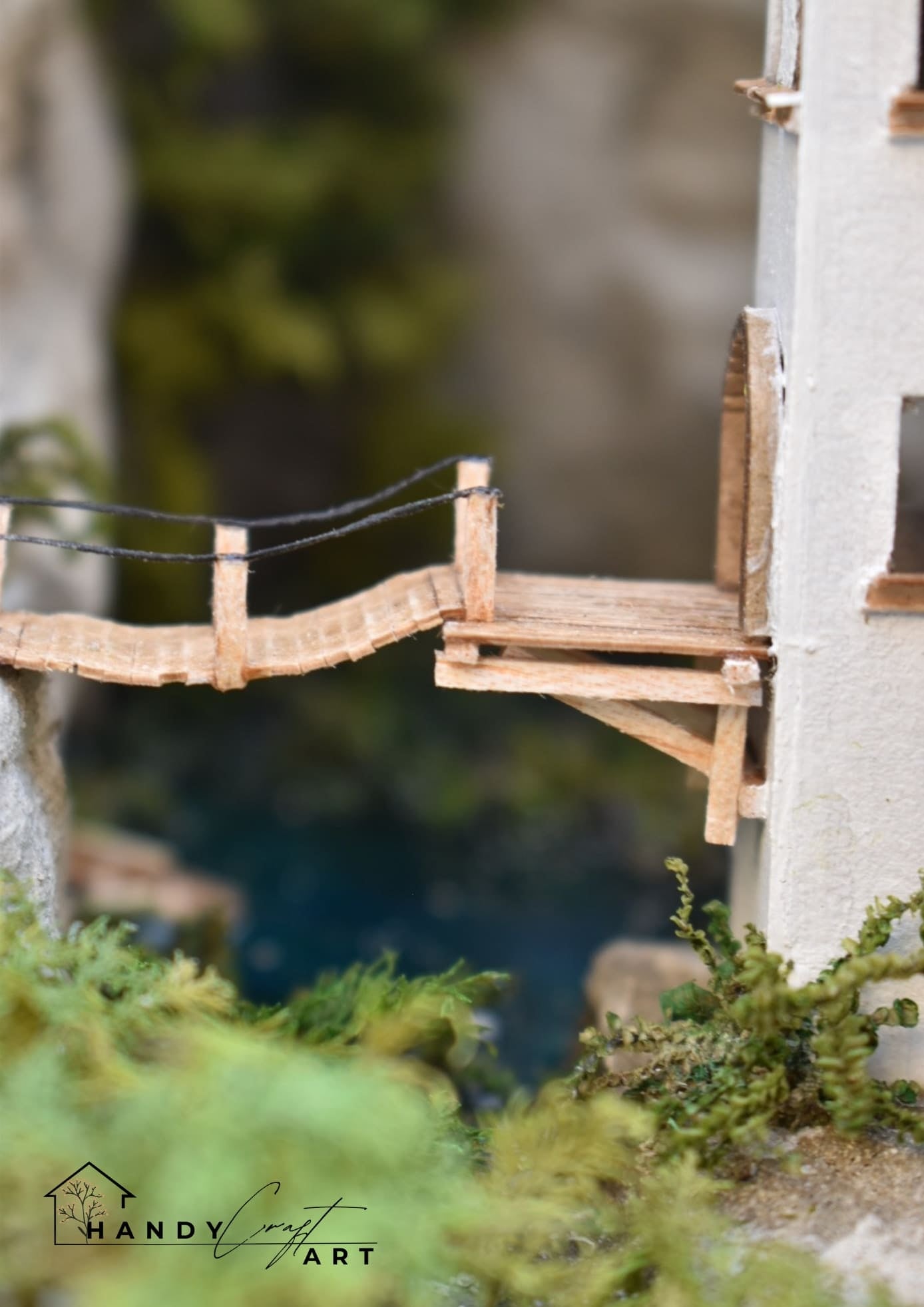 Miniature wooden bridge in the Book Nook with HandiCraftArt branding in a natural setting.