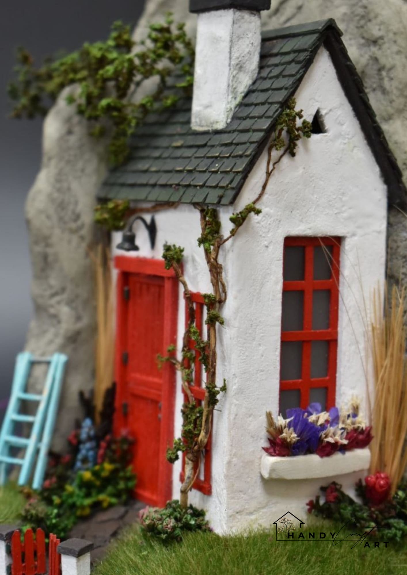 Miniature model of a Irish cottage with a red door and window, surrounded by greenery.